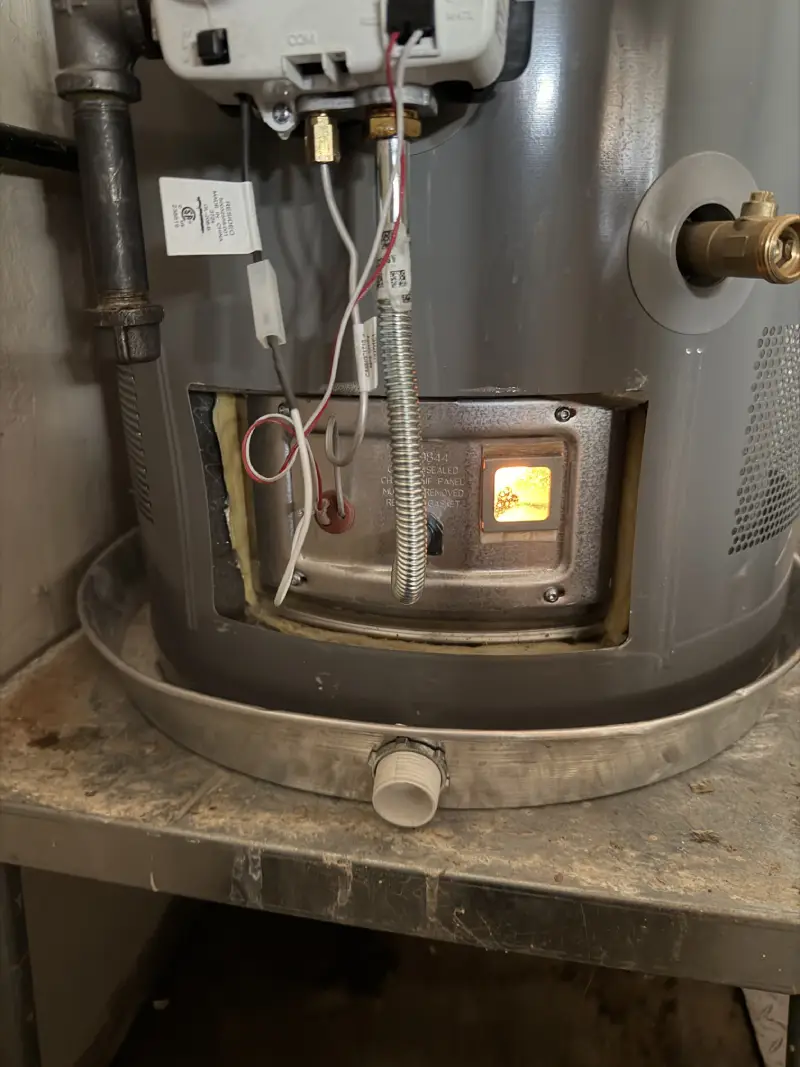 Gas water heater sight glass showing a yellow-orange burner flame caused by incomplete combustion